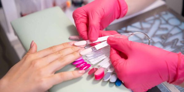 Nail master helps to select a nails color polish from the samples collection. A palette of transparent tips with different colors.