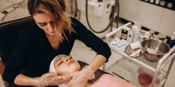 Young woman beautician is doing the cleaning procedure in the beauty salon. Face Skin Care. Cleansing Procedure. Cosmetology.